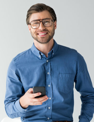 Confident businessman in blue shirt holding a smartphone, representing professional communication or mobile technology.