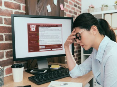 Concerned individual at a computer workstation with a security warning on the screen, indicative of a cybersecurity issue, data breach, or critical error requiring urgent attention.