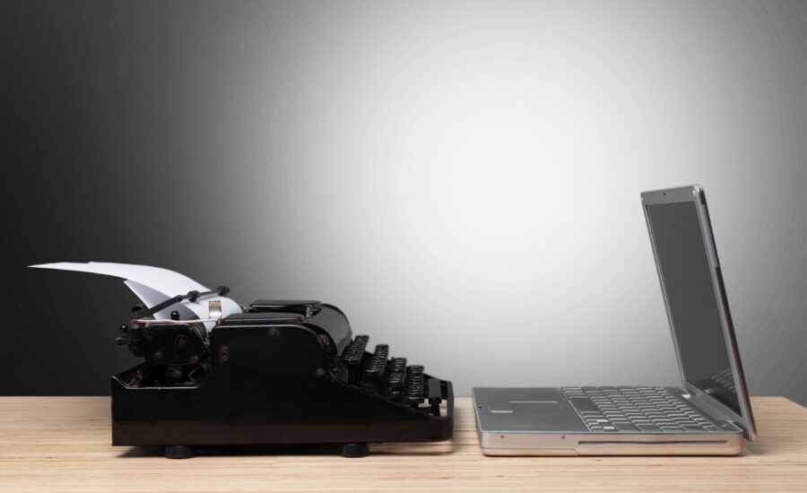 Vintage typewriter next to a contemporary laptop on a wooden desk, symbolizing the evolution of writing technology from mechanical to digital.