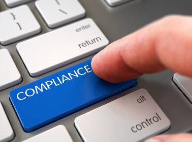 Finger pressing a blue 'COMPLIANCE' button on a grey keyboard, highlighting the importance of regulatory compliance in business practices and corporate governance.