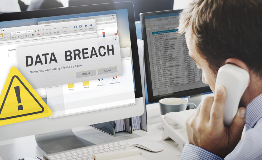 Concerned businessman on the phone viewing a computer screen with a 'Data Breach' alert and caution symbol, representing urgent cybersecurity issues in the workplace.