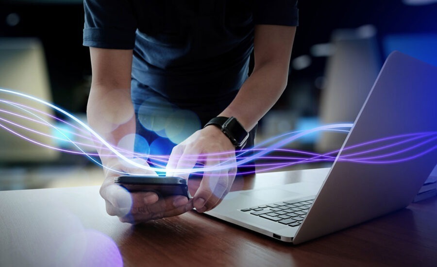 Person syncing smartphone with laptop, illustrated by vibrant purple and blue data streams, symbolizing seamless connectivity and data transfer technology.